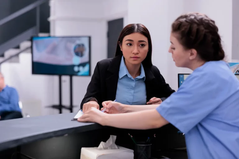 Una recepcionista de clínica atiende a una paciente y le da indicaciones