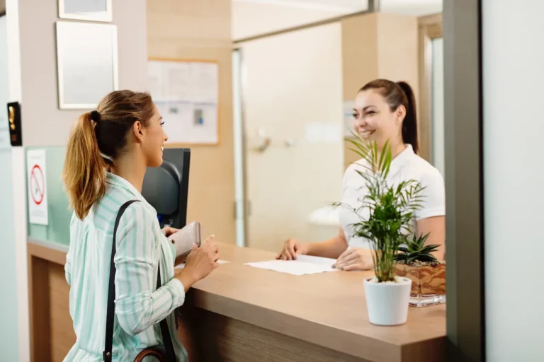 Mujer vestida de azul es atendida por una recepcionista detrás de un mostrador
